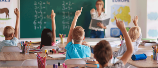 Teacher pointing to eager students wanting to learn in a classroom setting. 